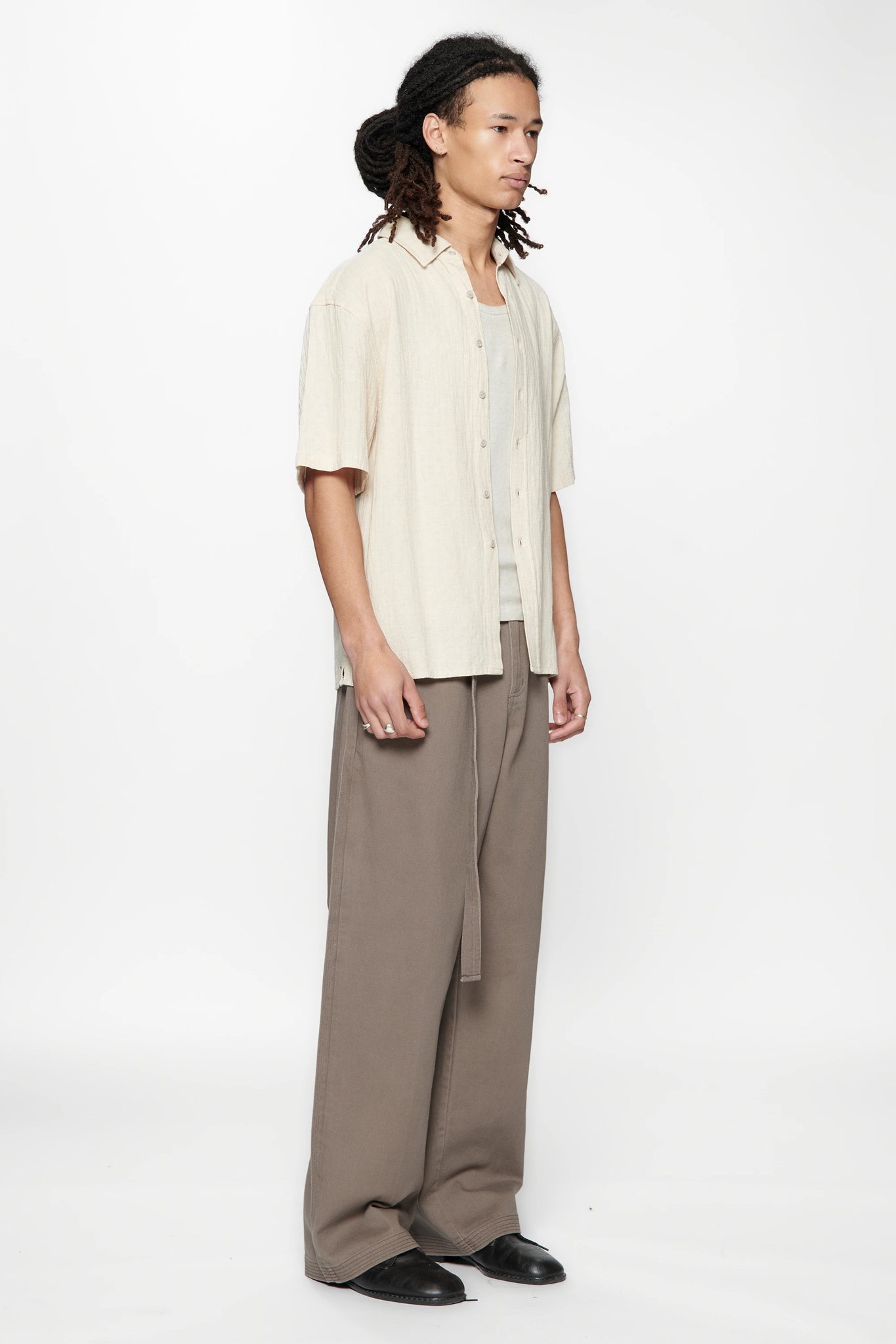 Side view of a person wearing the Hold SS Shirt in Off White and brown pants on a white background