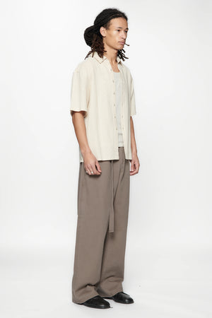 Side view of a person wearing the Hold SS Shirt in Off White and brown pants on a white background